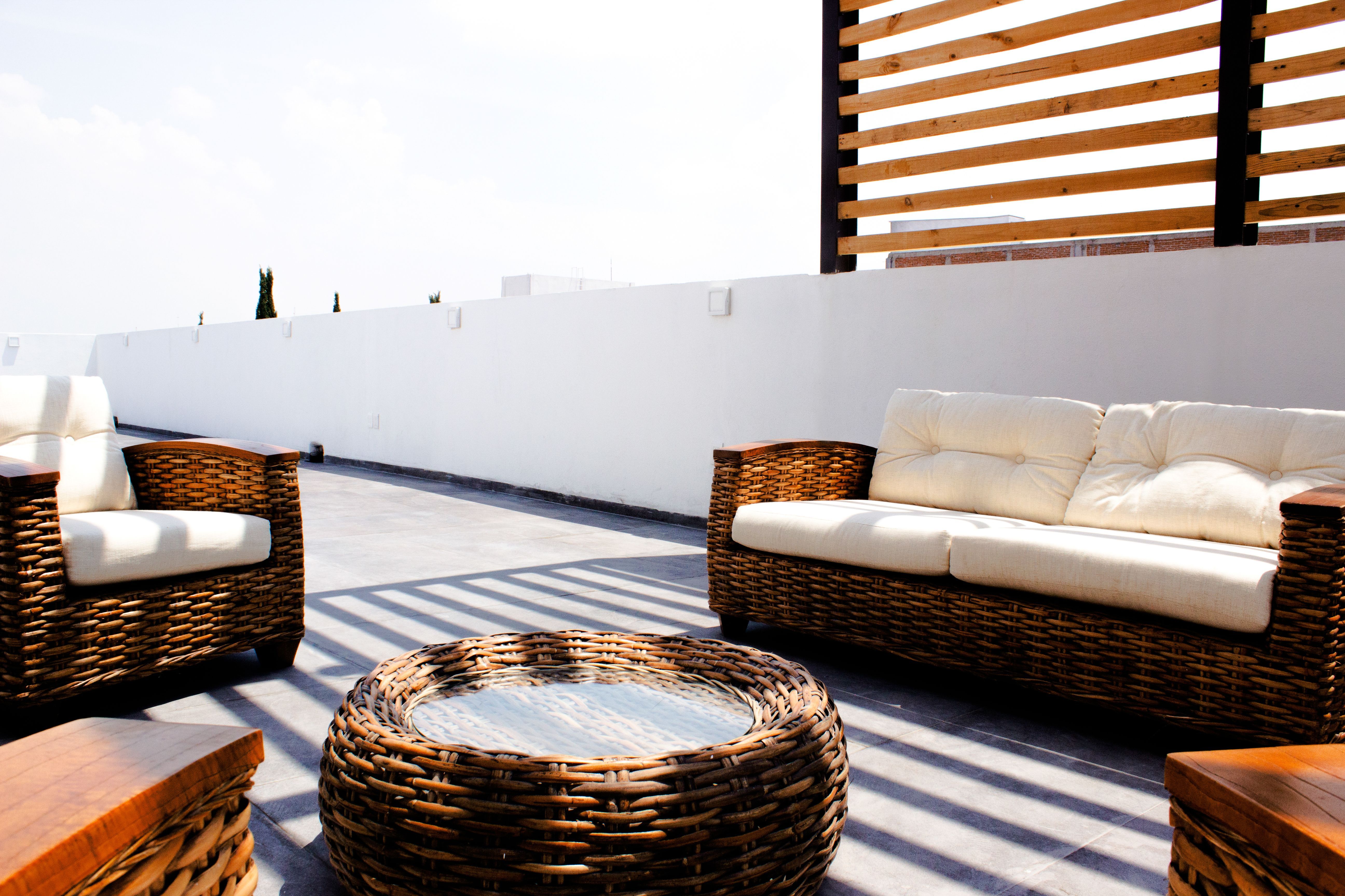 Terraço exterior com sofás de vime, mesa baixa e pérgola de madeira sobre pavimento de pedra